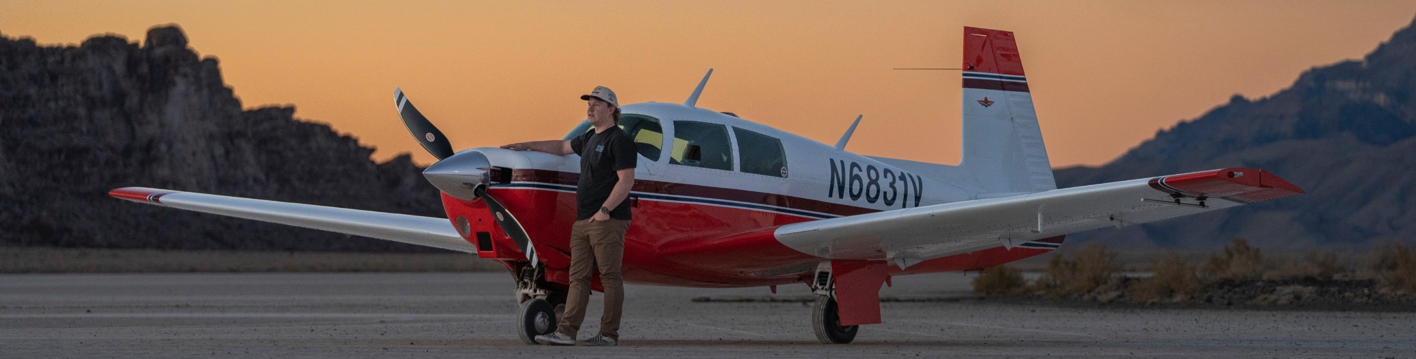 The red-and-white Mooney N6831V on the ground at sunset, with both wingtips, the tail and landing gear visible.